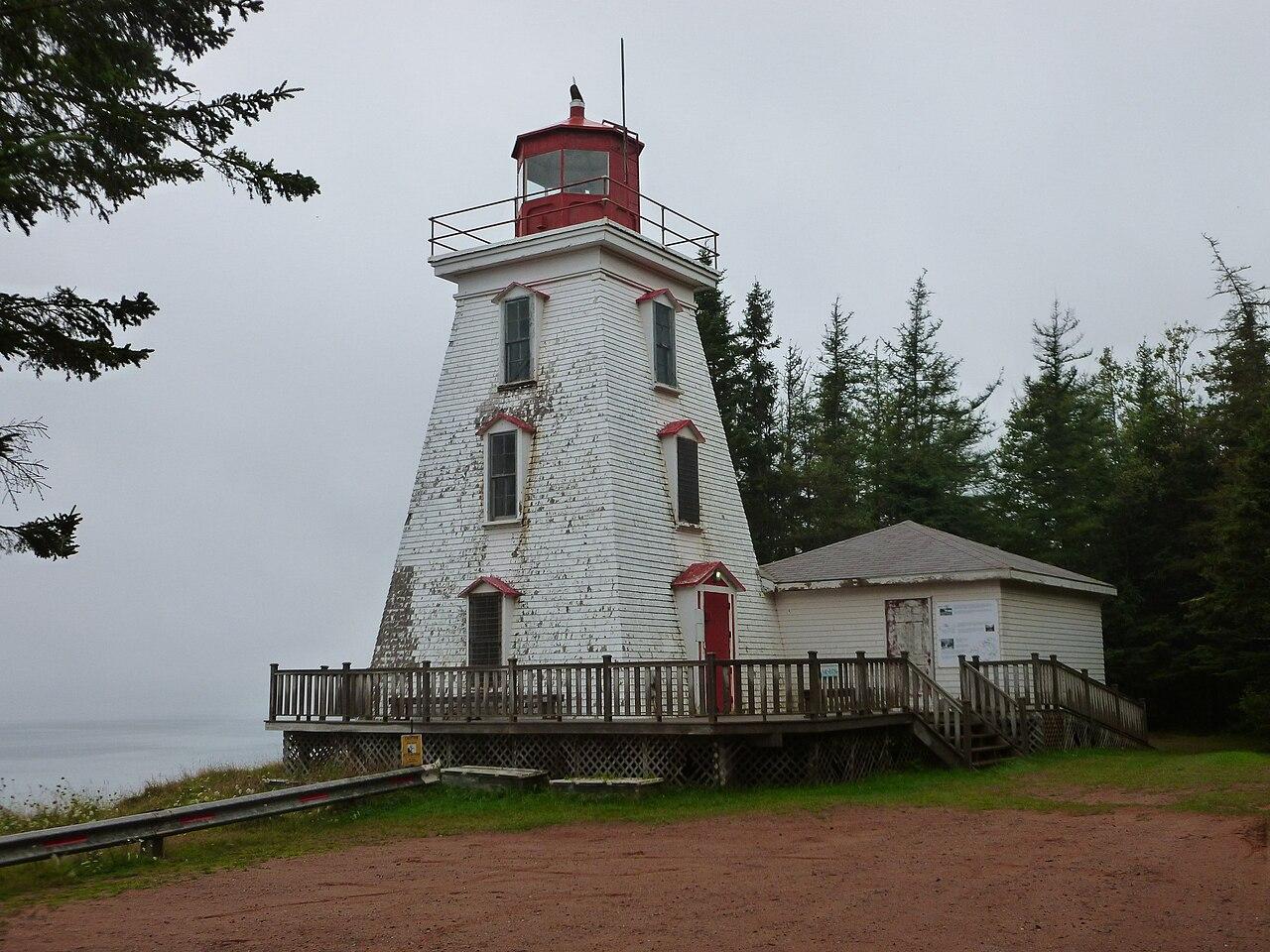 Cape Bear Lighthouse in fog, with spruce trees and a red dirt drive