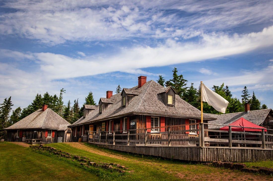 Reconstructed wooden buildings at Roma at Three Rivers, with grey shingle roofs and red window trim