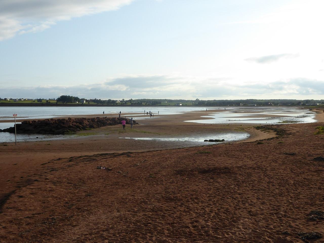 Red sand beach at low tide just west of Souris, with a rock breakwater and the far shore